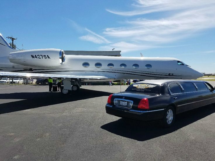A rear-angle view of a polished black stretch limousine from the SRB Limo fleet parked directly next to a white private jet on an airport tarmac under a bright blue sky