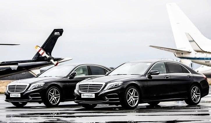 Two polished black executive Mercedes-Benz sedans from the SRB Limo fleet parked side-by-side on an airport tarmac with the wings and tails of private jets visible in the background.
