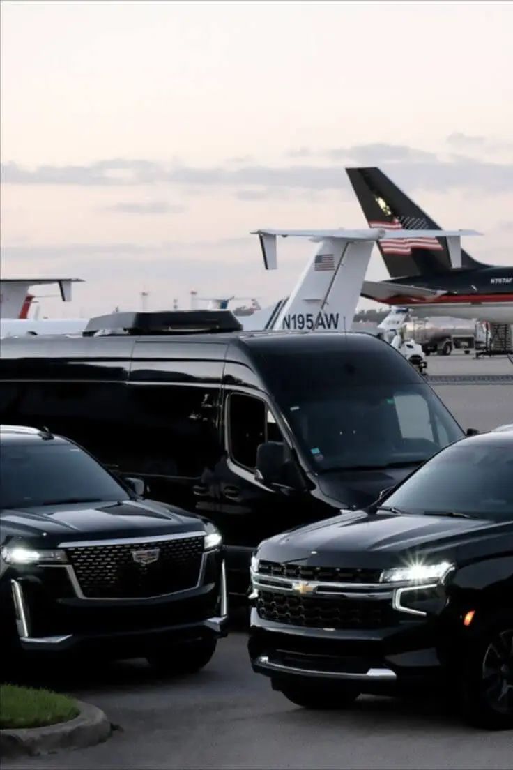 A group of polished black luxury vehicles from the SRB Limo fleet, including a Cadillac Escalade, a Chevrolet Suburban, and a high-roof executive van, parked on an airport tarmac with the tails of private jets visible in the background.