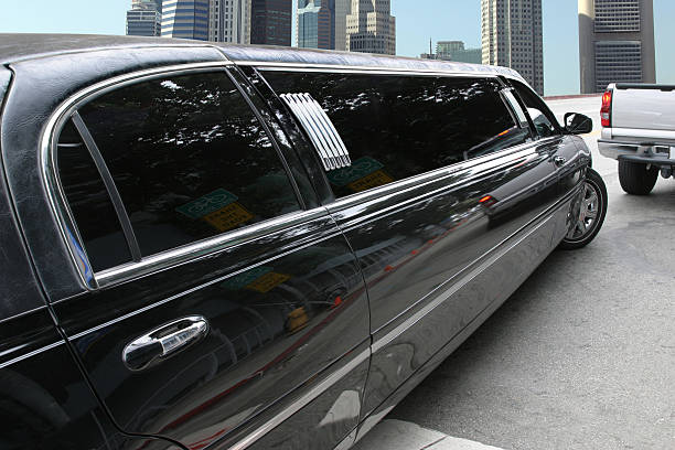 A close-up side view of a polished black stretch limousine from the SRB Limo fleet parked on a city street with tall buildings in the background.