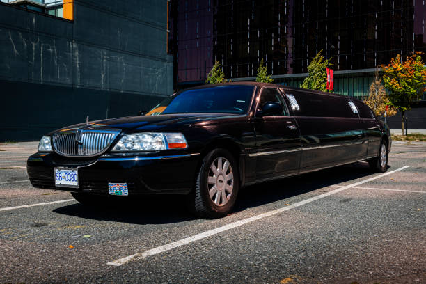 A front-angle view of a long black Lincoln Town Car stretch limousine from the SRB Limo fleet parked in a sunny outdoor lot with modern buildings in the background.