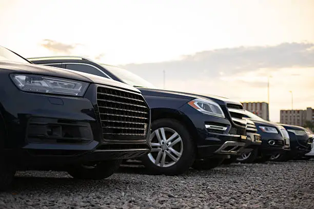 A row of polished black and dark blue luxury SUVs from the SRB Limo fleet parked on a gravel surface under a soft evening sky.