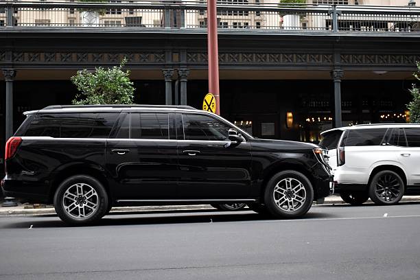 A side profile of a polished black luxury SUV from the SRB Limo fleet parked on a city street in front of a building with classic architectural details.