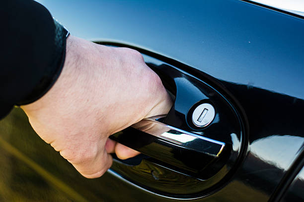 A close-up shot of a chauffeur's hand in a black sleeve opening the chrome door handle of a polished black luxury vehicle.