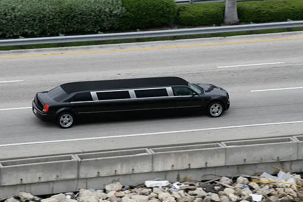 A high-angle side view of a long black stretch limousine from the SRB Limo fleet cruising along a multi-lane highway next to a roadside barrier