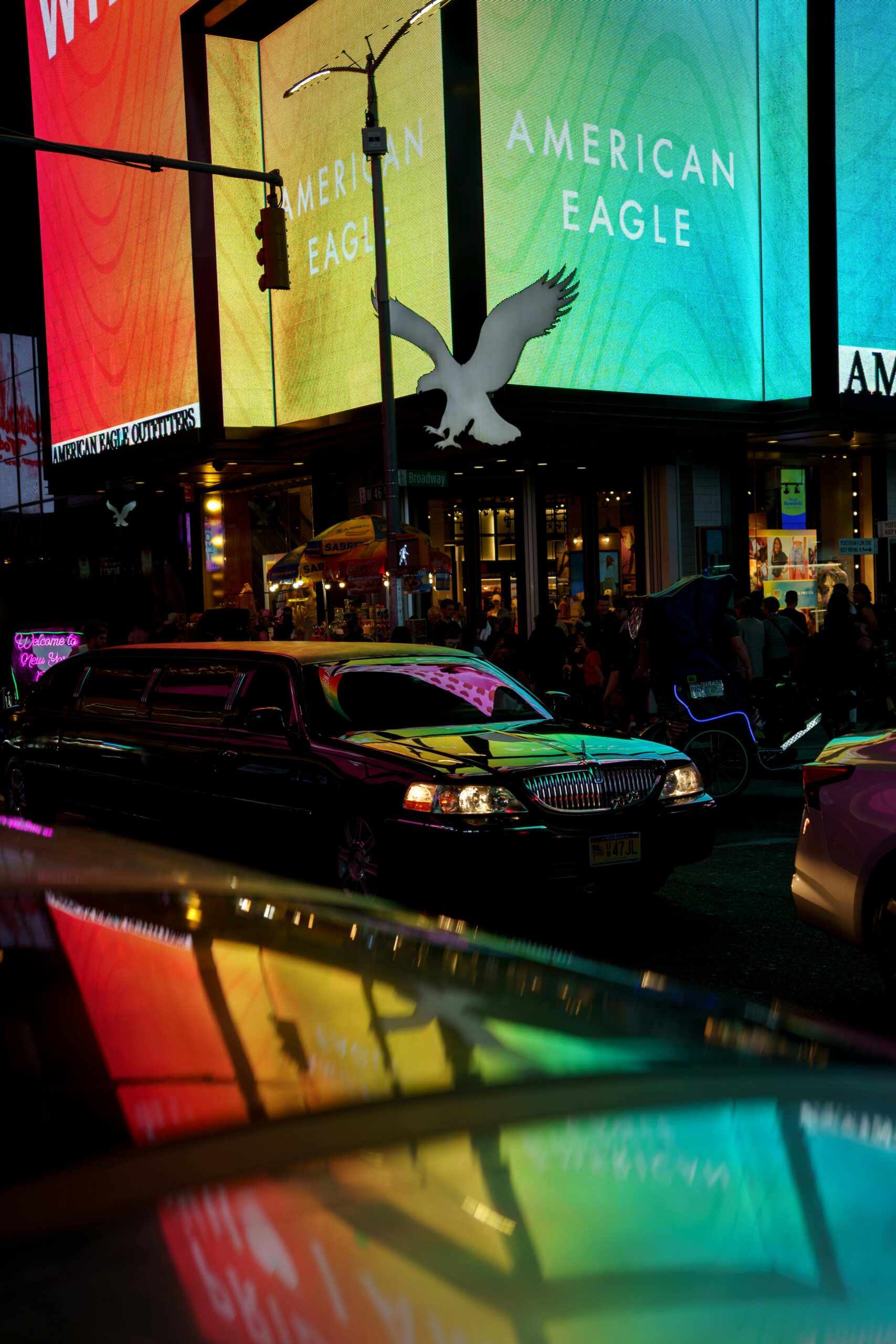 A long black SRB Limo stretch limousine driving through a brightly lit city center at night with colorful neon billboards in the background
