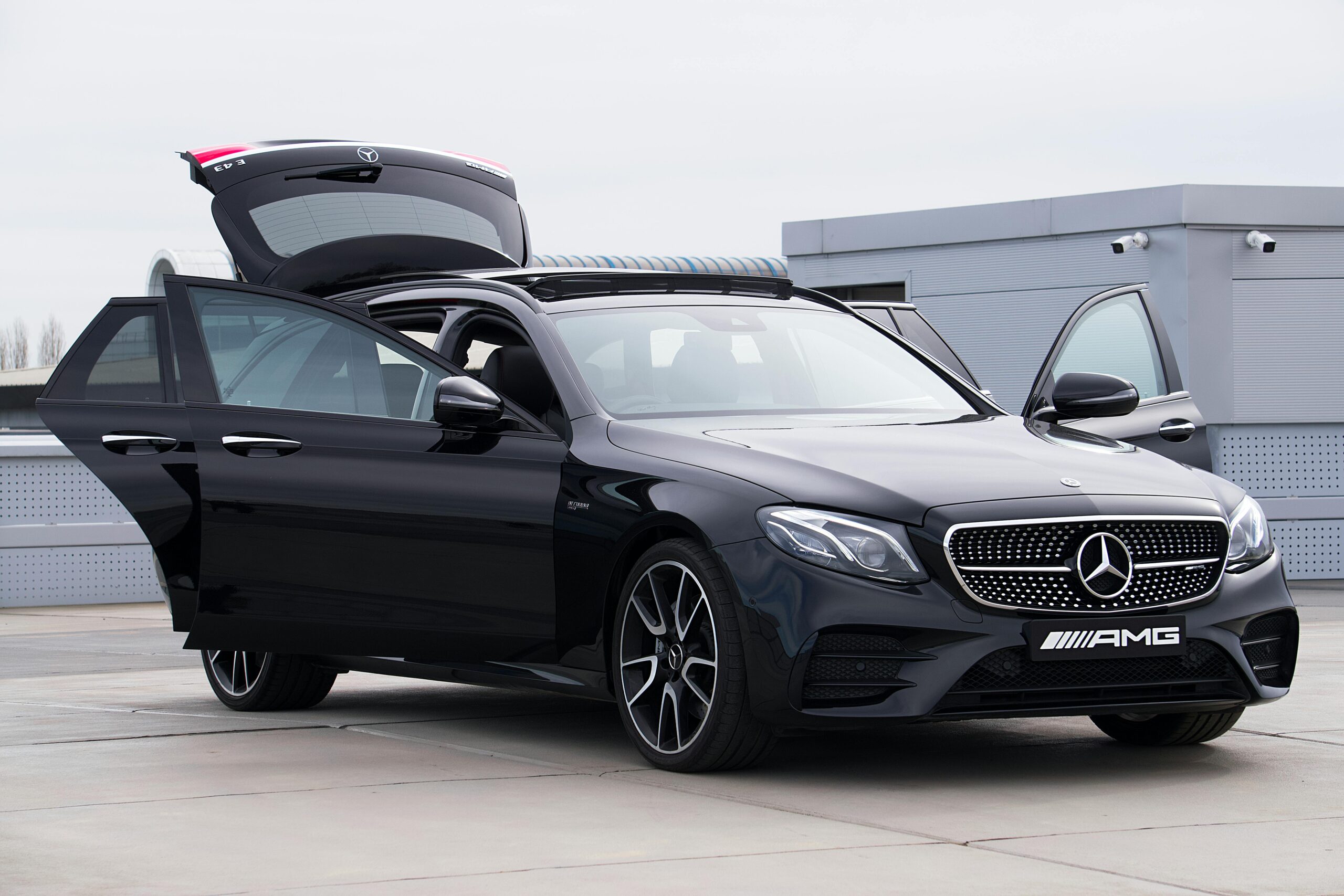 A polished black Mercedes-Benz AMG sedan with open doors and trunk, showcasing a spacious interior and cargo area for professional transportation.