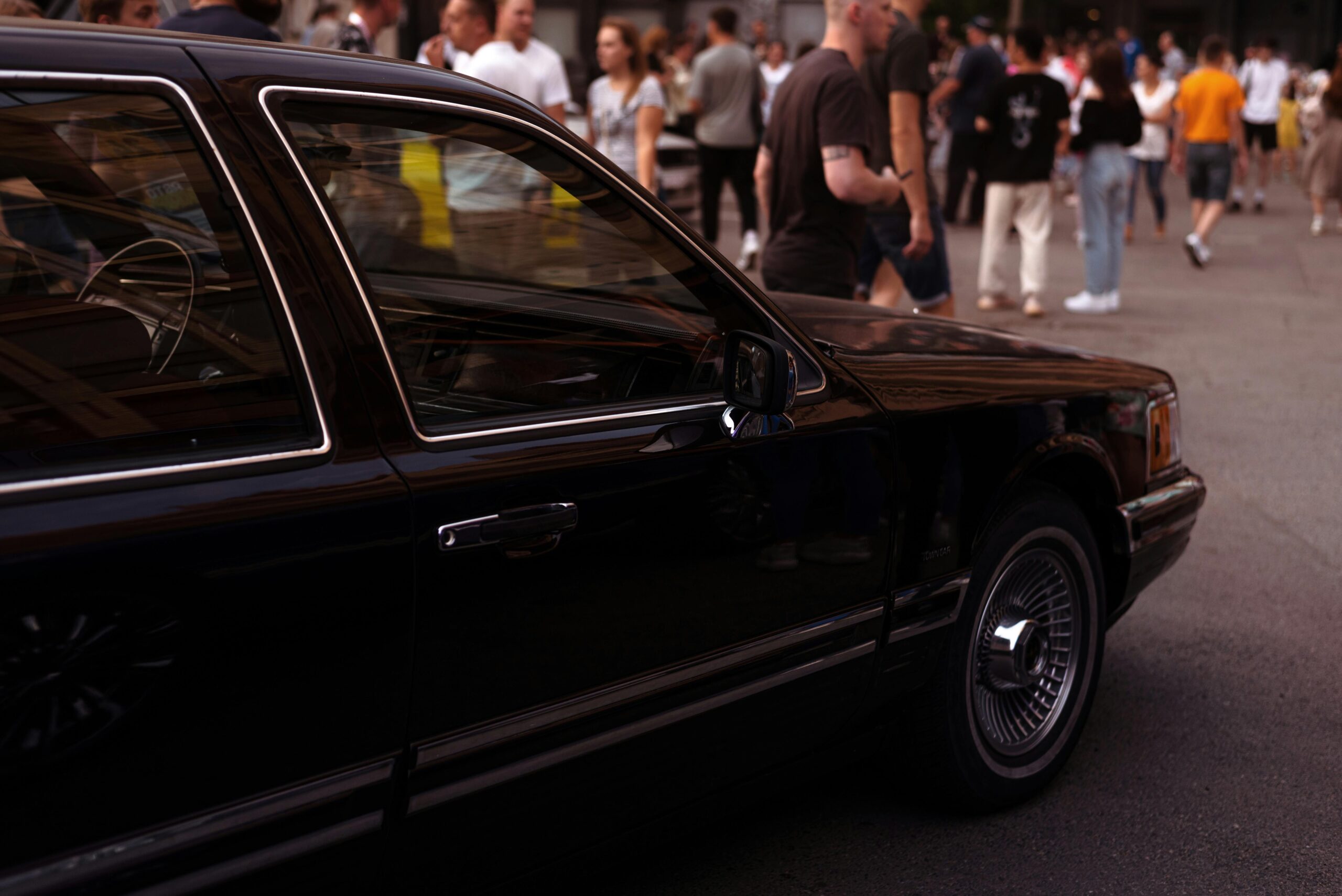 Classic black SRB Limo sedan parked on a busy city street with people in the background, representing reliable transportation for urban events and sightseeing