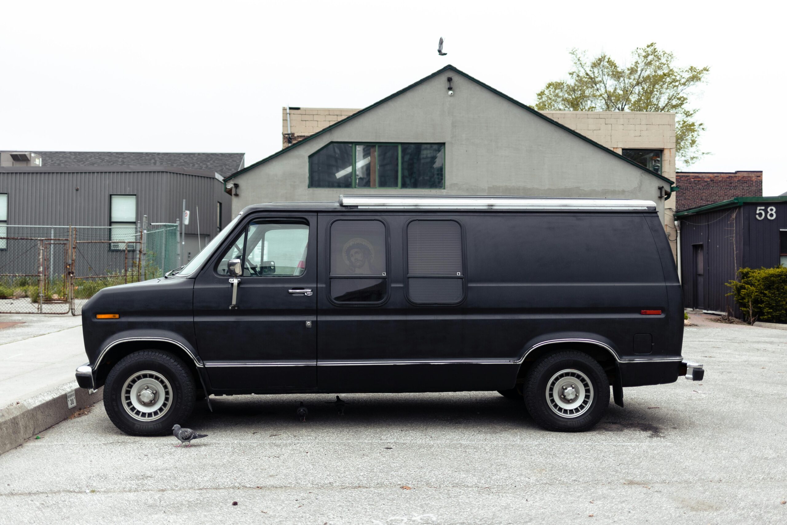 A side profile of a matte black high-capacity passenger van from the SRB Limo fleet parked in an urban area, featuring tinted windows and a clean, professional aesthetic.